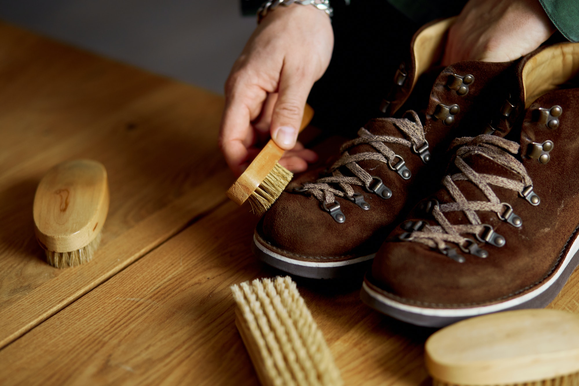 man s hand clean suede shoes boots with a brush on wooden background