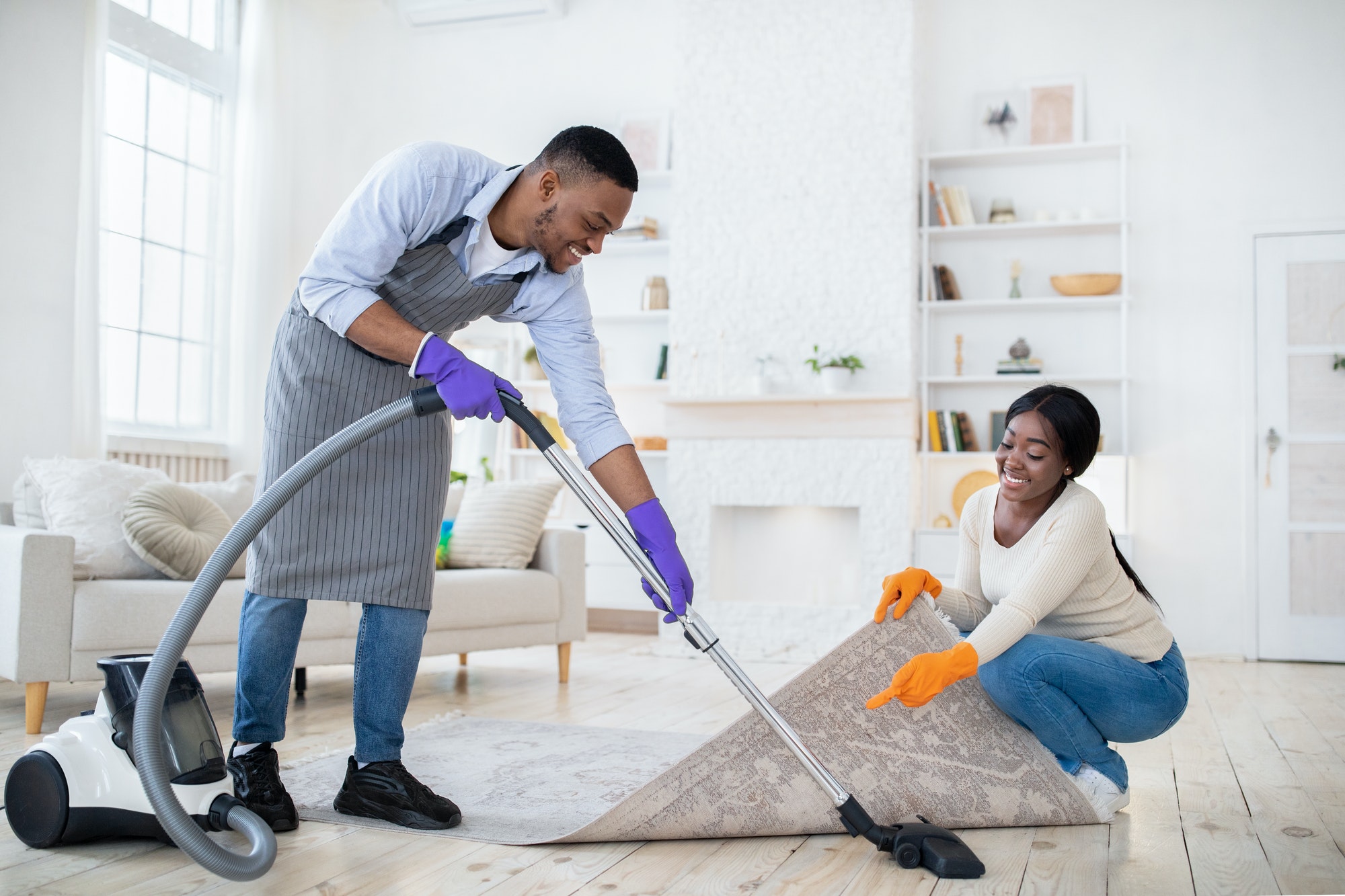 positive black couple cleaning up together vacuuming under carpet at their house copy space